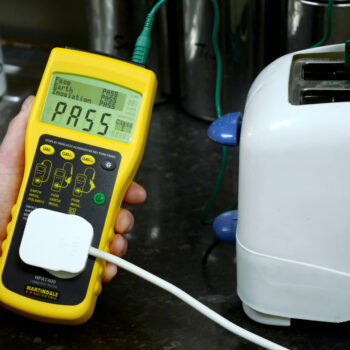 A technician performing PAT testing on a toaster using a handheld electrical testing device, ensuring compliance with safety regulations in Lancaster. This process is essential for landlords, businesses, and public spaces to maintain electrical safety and meet legal requirements.