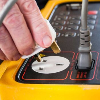 Close-up of a hand connecting a plug into a PAT testing device, illustrating PAT testing procedures for electrical safety in Lancaster. Essential for businesses, landlords, and public spaces to ensure compliance with health and safety regulations. Services include PAT testing, PAT tester in Lancaster, and electrical testing to prevent hazards and maintain safety standards.